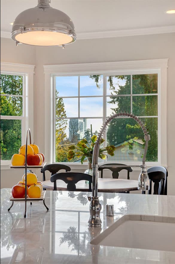 Interior view of a kitchen dining area with a large window, pendant light, and island countertop.