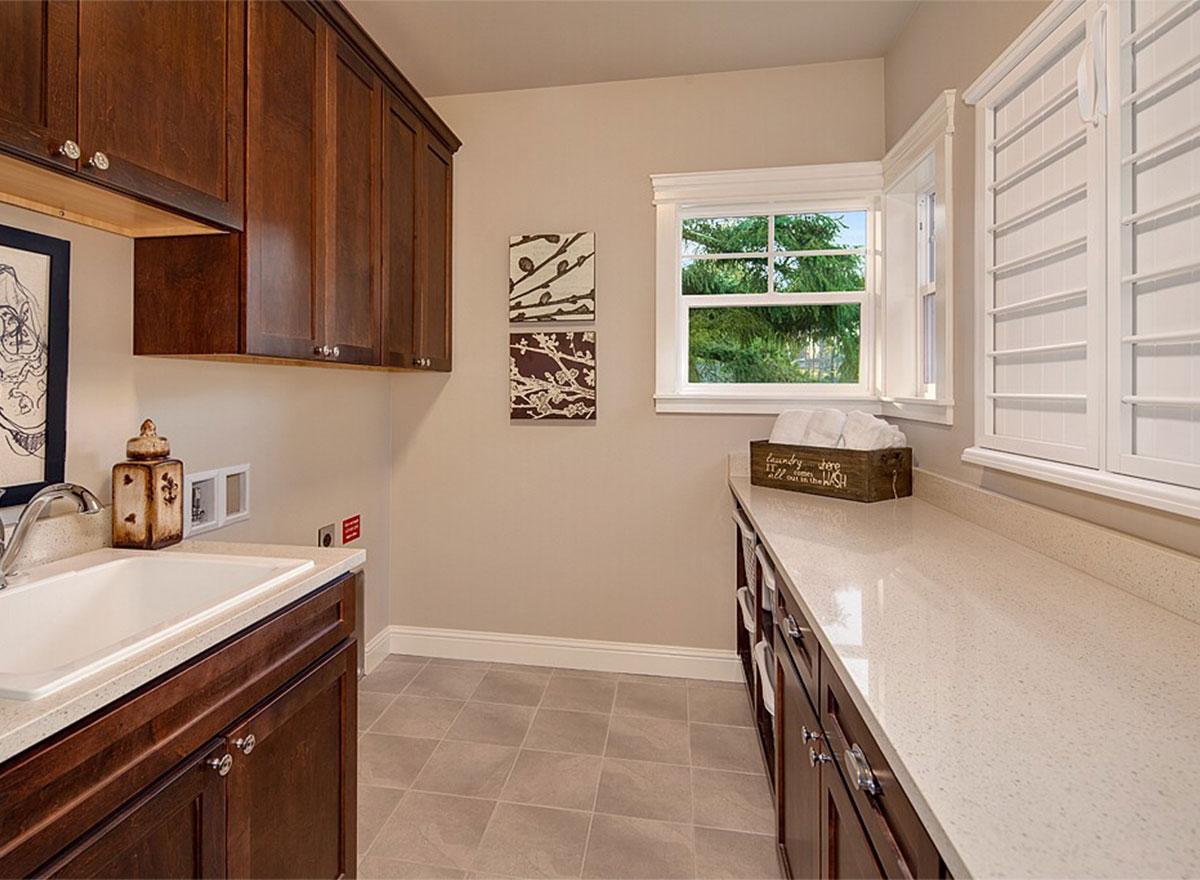 Laundry room with dark wood cabinets, white quartz countertop, sink, and window.