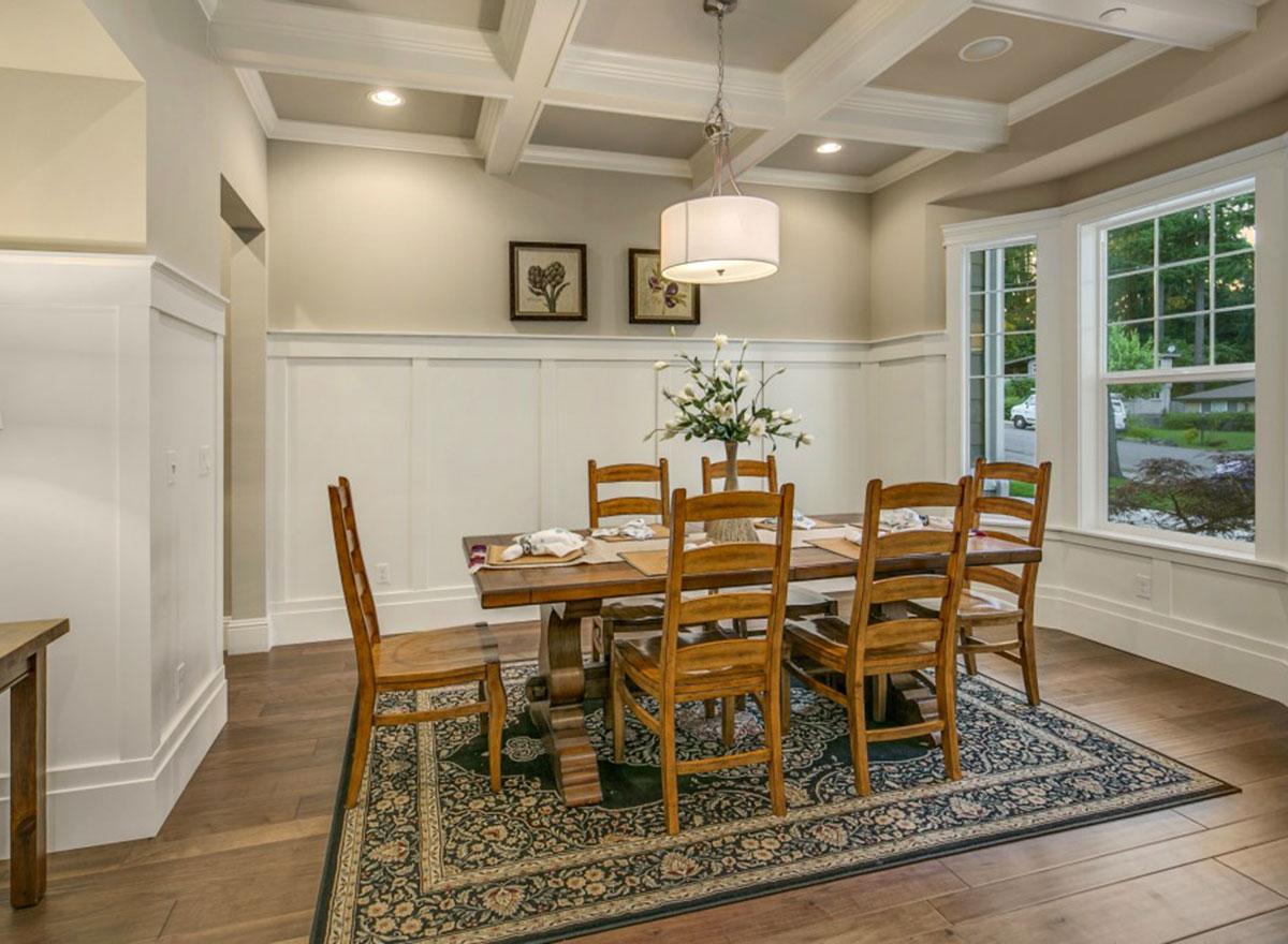 Dining room with coffered ceiling, wainscoting, large windows, and wooden dining set.