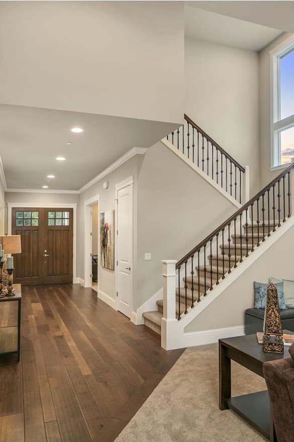 Foyer with double wooden door, hardwood floors, and a staircase with black spindles and dark wood railing.