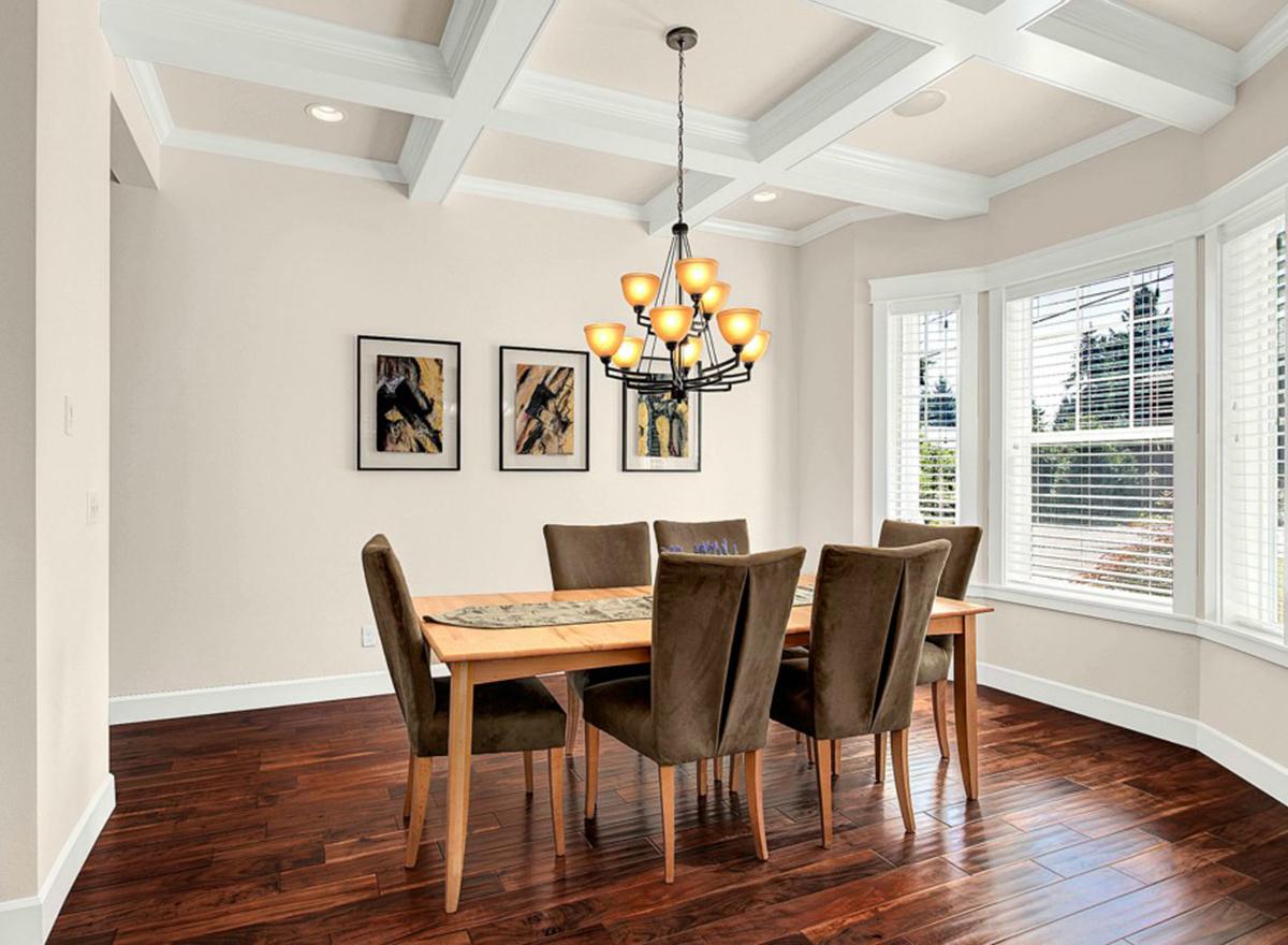 Dining room with coffered ceiling, wood floors, bay windows, and a table set for six.