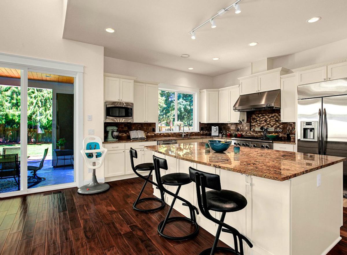 Kitchen with white cabinets, granite-topped island, stainless steel appliances, and sliding glass doors to patio.