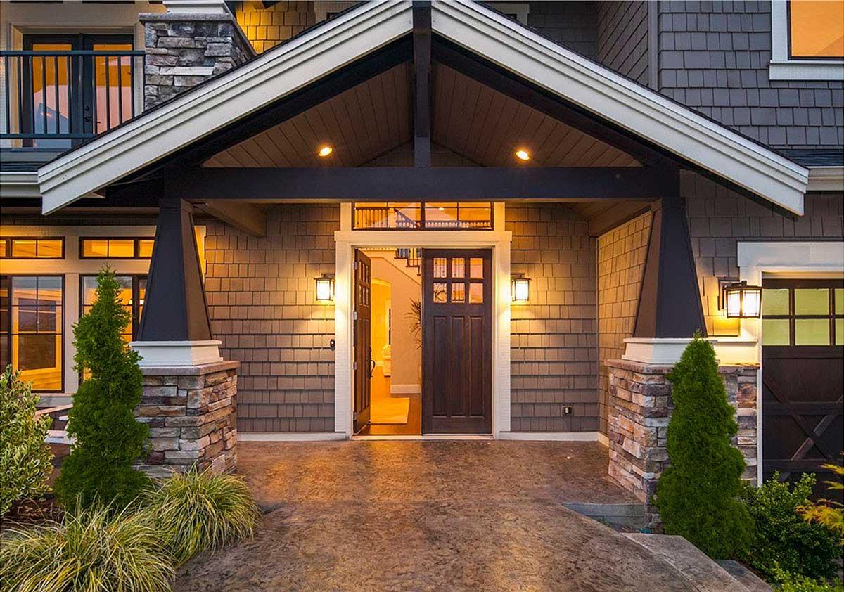 House plan exterior with stone pillars, a prominent gabled entryway, and double entry doors. The siding features horizontal shingles.