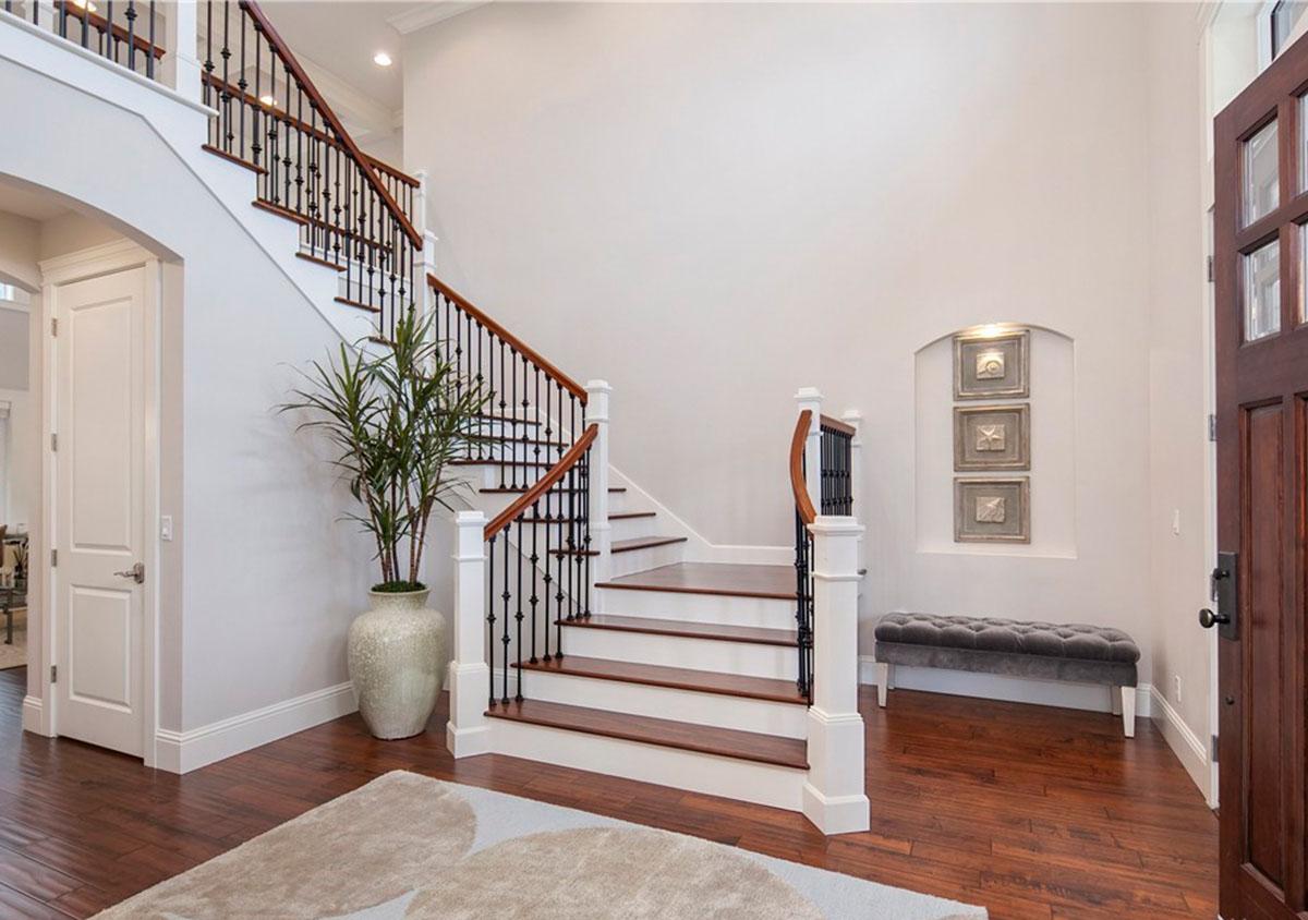 Interior view of grand staircase with wooden treads and black balusters, flanked by a plant and entry door.