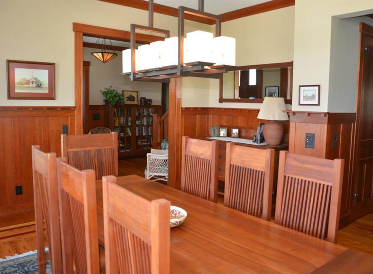 Dining room with wood wainscoting, a long table with chairs, and a view into a library with a bookshelf.
