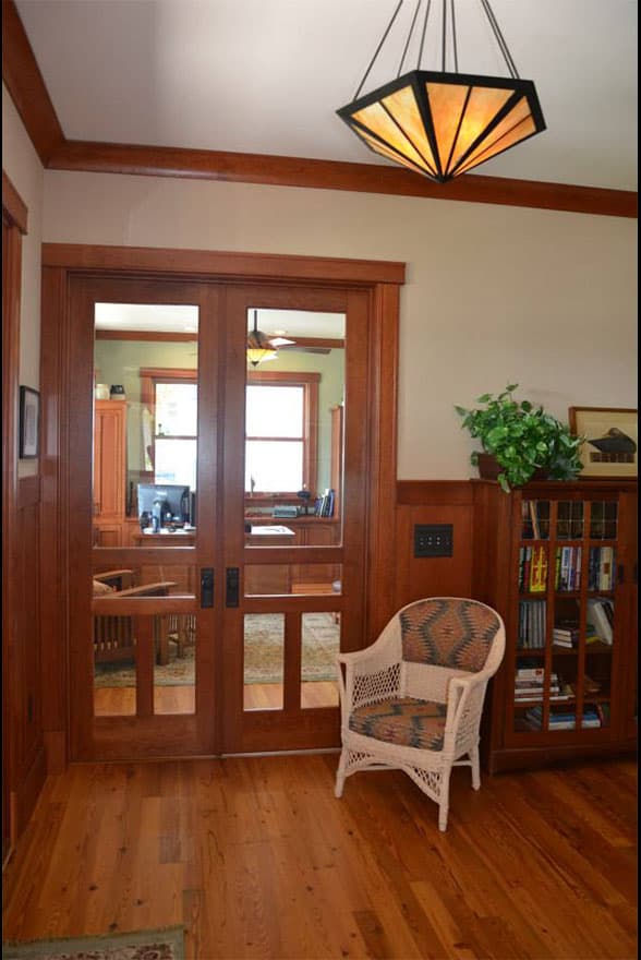 Interior view of office space with double glass-paneled doors, built-in bookshelves, and a wicker chair.