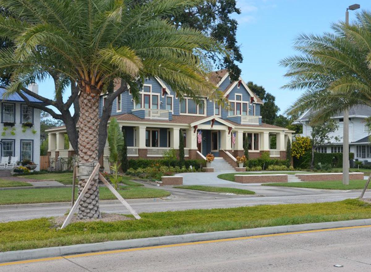 Blue two-story house plan with prominent front porch, gables, dormers, and multiple balconies. Features red-trimmed windows.