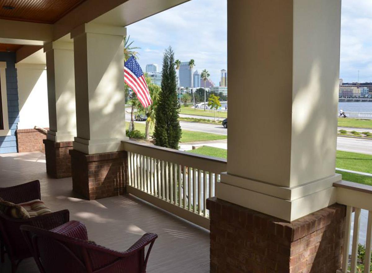Porch exterior with brick base columns and white railings overlooking a city skyline and water.
