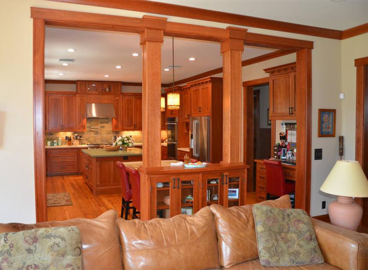 Open concept interior with kitchen, island, and desk area. Features wood cabinetry, columns, and seating.