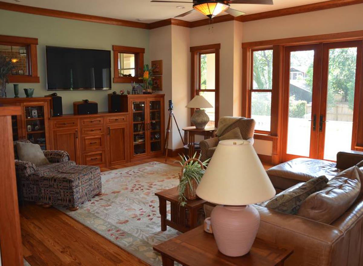 Living room with built-in cherry wood entertainment center, patterned armchair, leather sofa, and large windows.