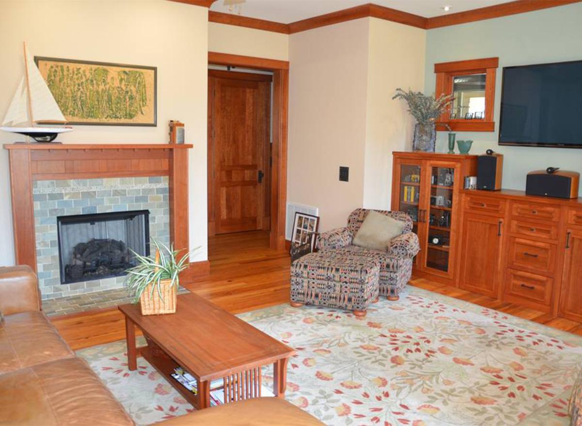 Living room with fireplace, wood paneling, built-in cabinetry, ottoman, and coffee table.