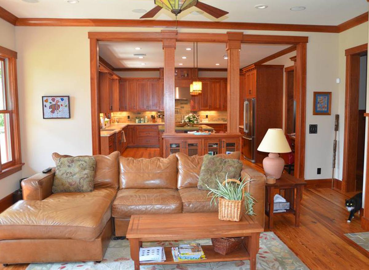 Living area with leather sectional sofa and adjoining kitchen with wood cabinetry, visible through wood-trimmed openings.