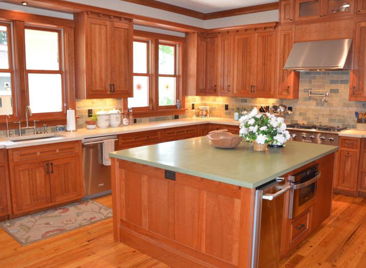 Kitchen with warm wood cabinetry, a central island with a green countertop, stainless steel appliances, and natural light from multiple windows.