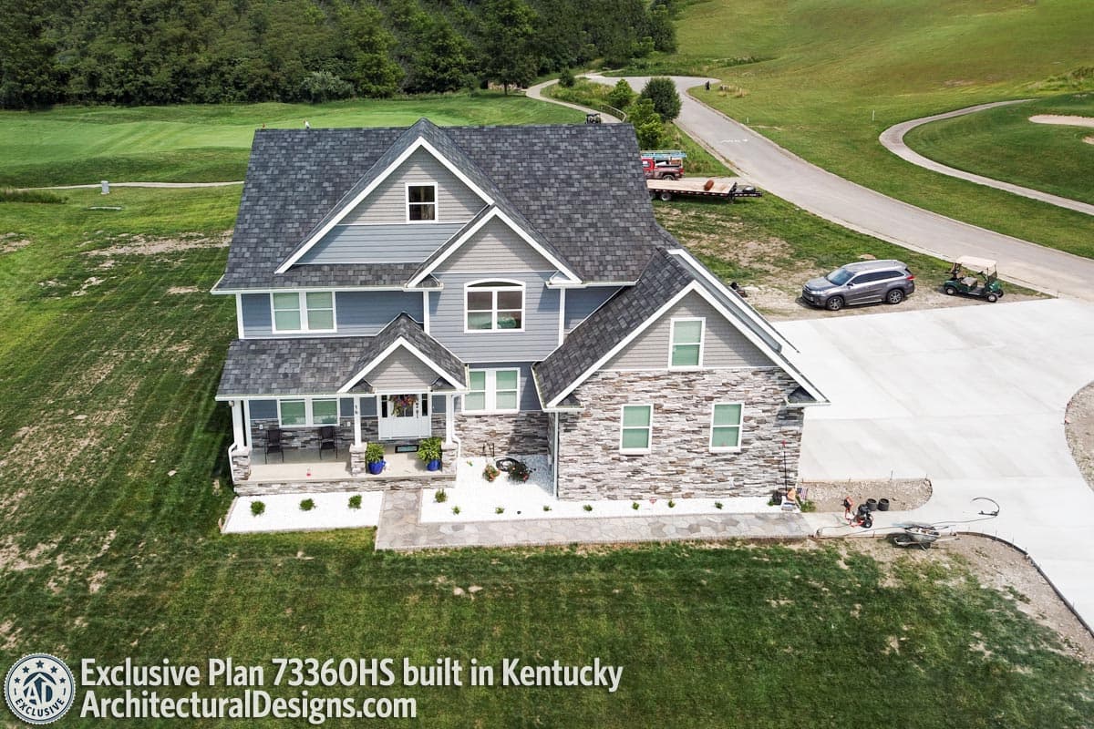 Two-story house plan exterior with a covered front porch, stone veneer accents, multiple gables, and dormer windows.