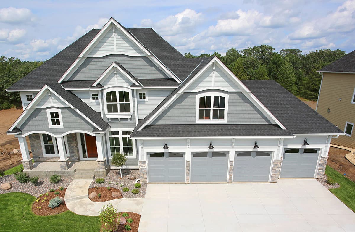 House plan exterior: Two-story Modern Farmhouse with multi-level gables, stone-accented entrance porch, and four-car garage.