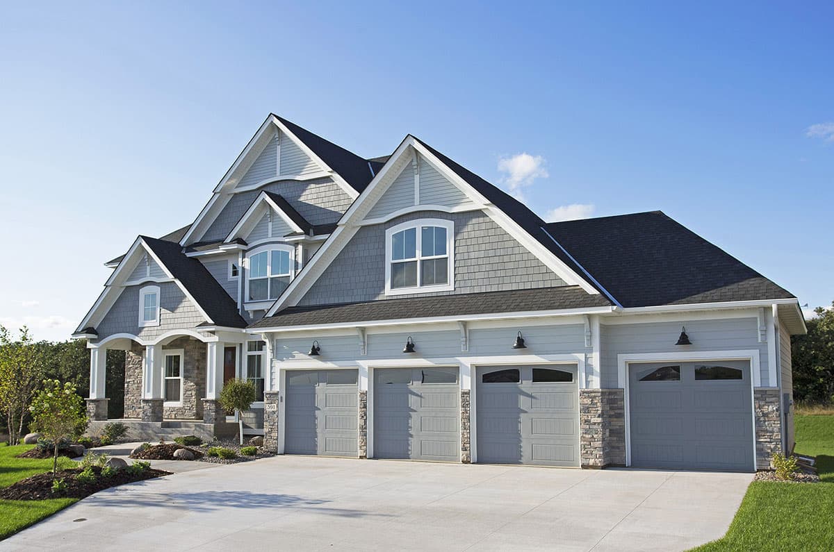 House plan exterior with stone accents, gables, arched dormers, and a four-car garage.