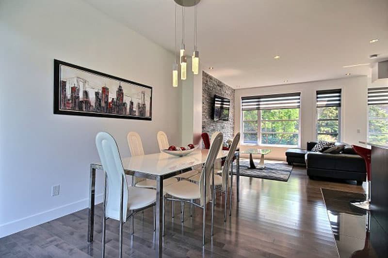 Open concept living and dining area with seating for six, stone accent wall, and large windows.