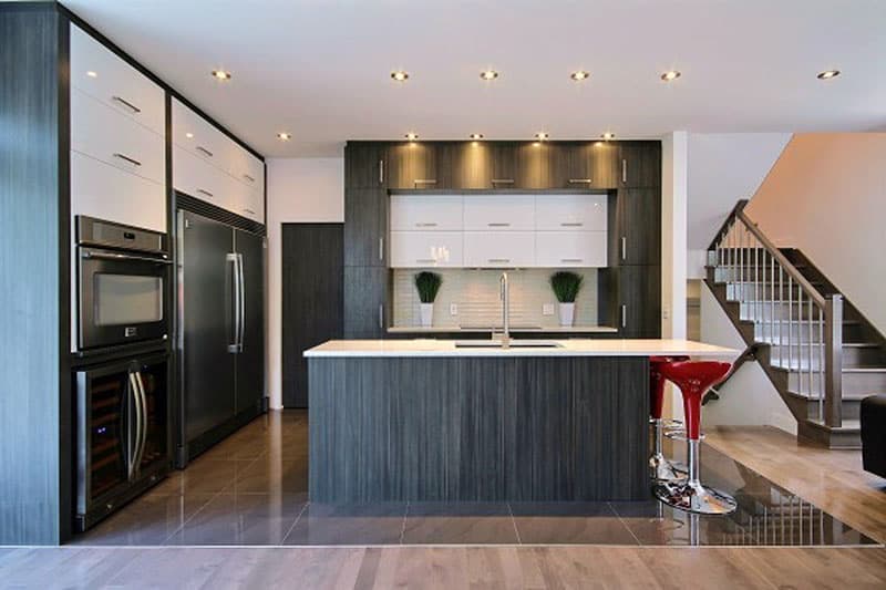 Modern kitchen with island, integrated appliances, dark wood cabinetry, and staircase leading to upper level.