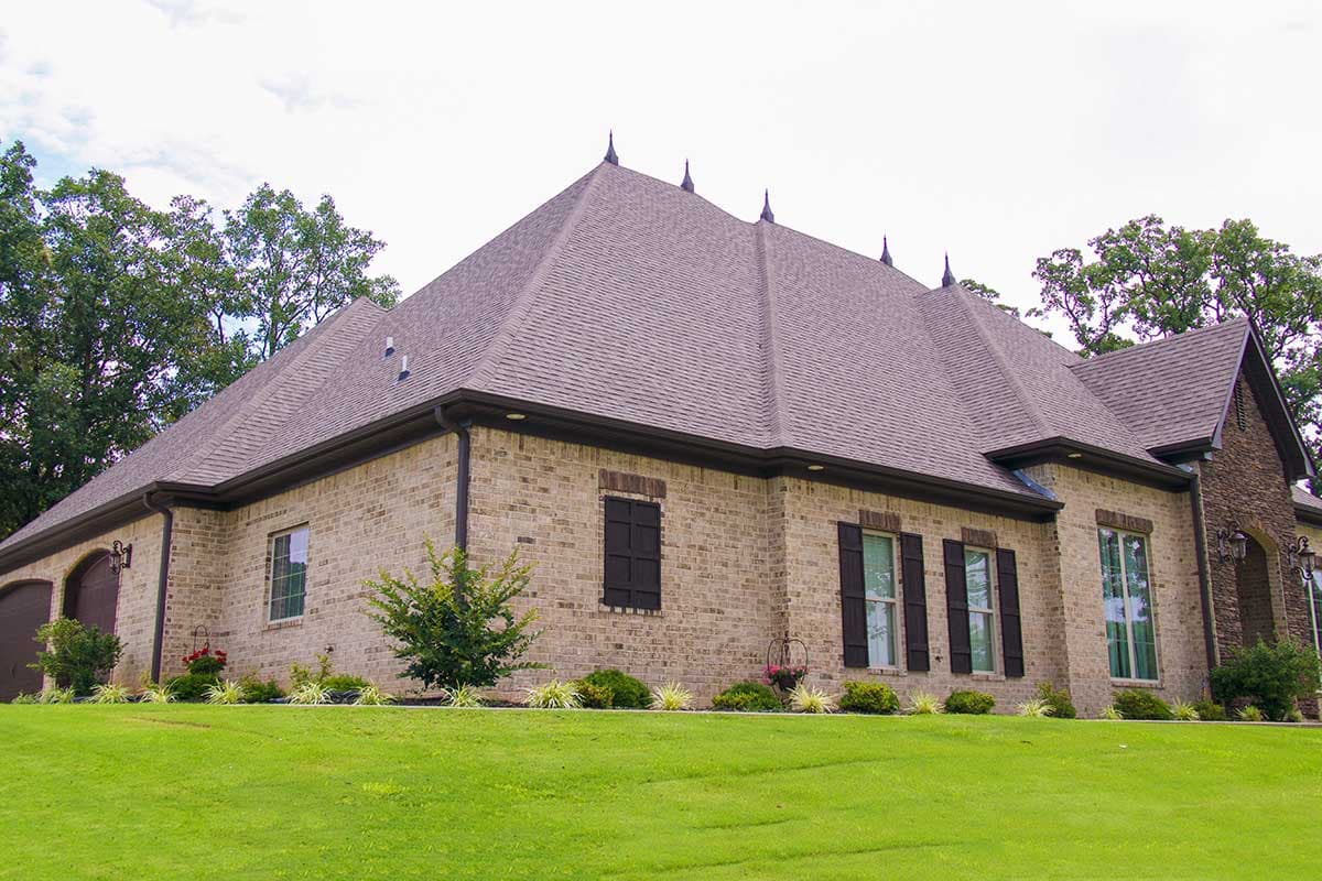 House plan exterior with multiple gables, brick facade, arched garage doors, and decorative roof finials.