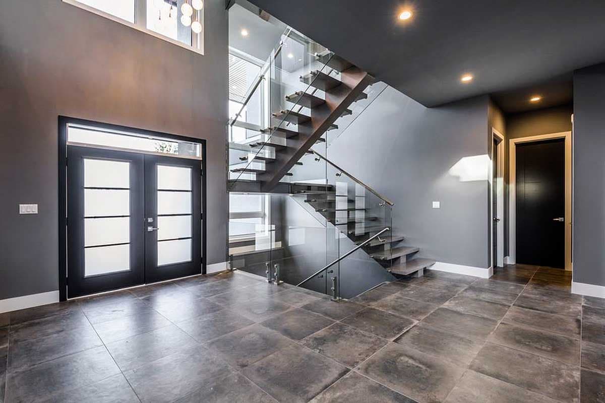 Modern interior foyer with floating wood stairs, glass railings, and double doors.