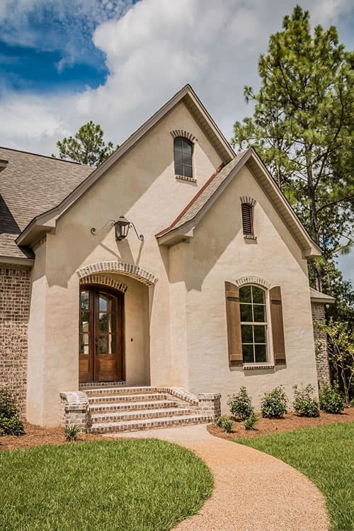 House plan exterior: French Provincial style, stucco finish, arched entryway, brick steps, prominent gables with dormers.