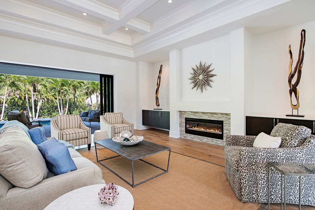 Living room with coffered ceiling, gas fireplace, and large sliding glass doors opening to a tropical patio.
