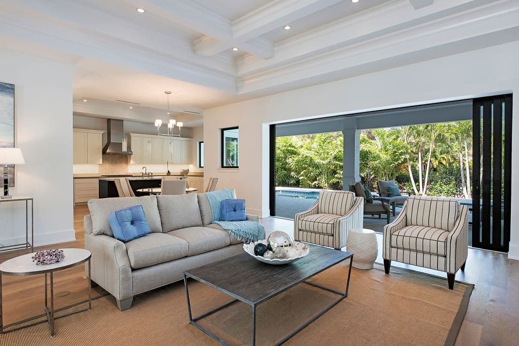 Open-plan living area with coffered ceiling, kitchen, and view of covered lanai with pool.