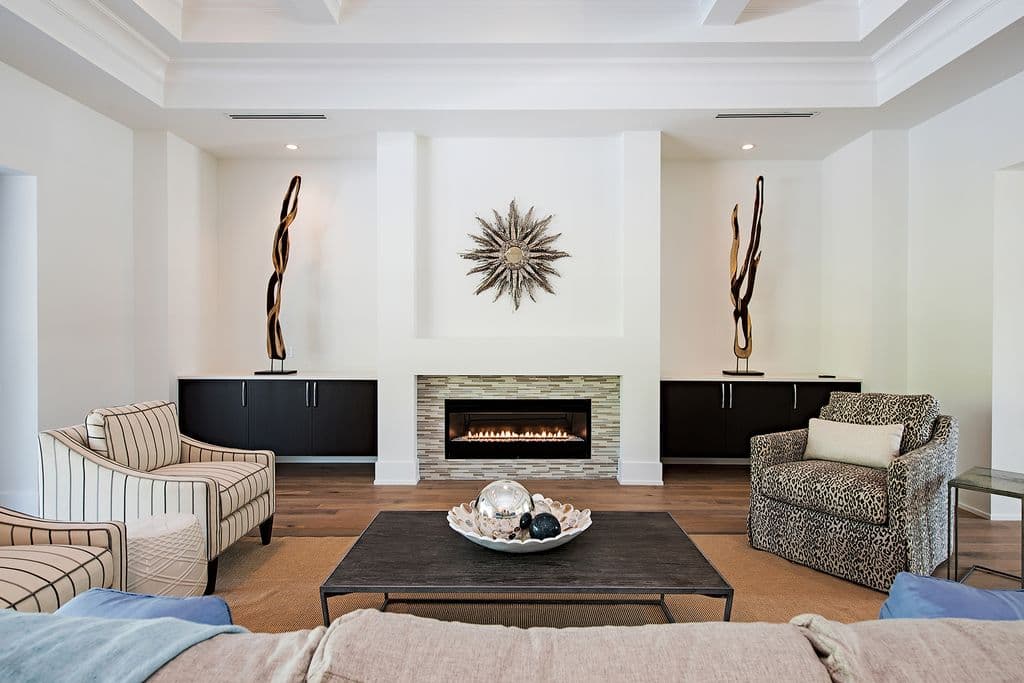 Living room interior with modern fireplace, built-in cabinets, coffered ceiling, and patterned armchairs.