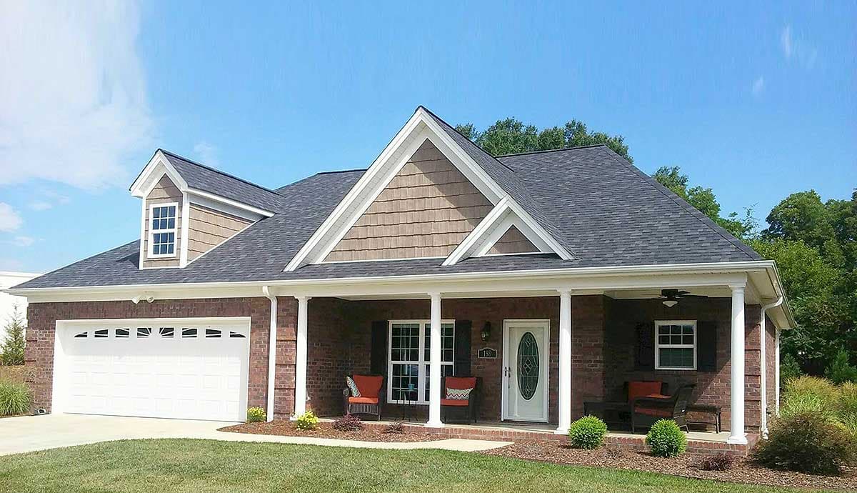 House plan exterior: brick ranch with covered front porch, gable dormer, and attached two-car garage.