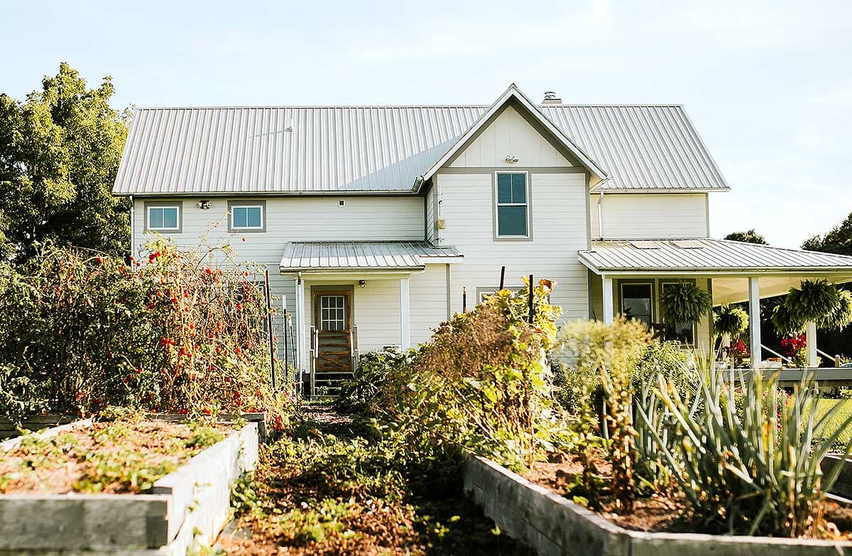House plan exterior: Two-story modern farmhouse with metal roof, gables, dormers, front porch, and attached garage.