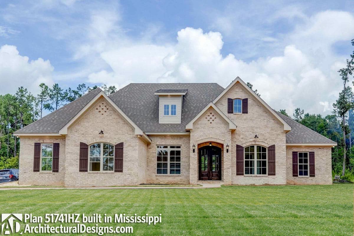 House plan exterior: light brick, two stories, arched entry, multiple gables, and dormer.
