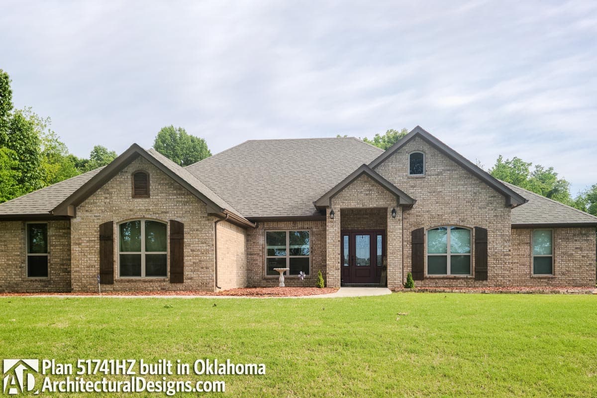 House plan exterior: One-story brick home with prominent gables, a covered entry with double doors, and arched windows with shutters.