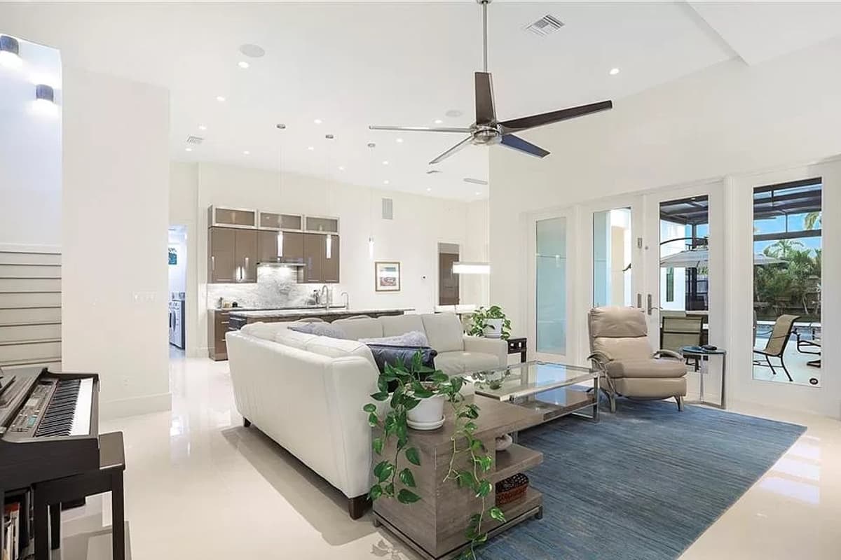 Open concept living area with a white sectional sofa, glass coffee table, large ceiling fan, and access to a patio.