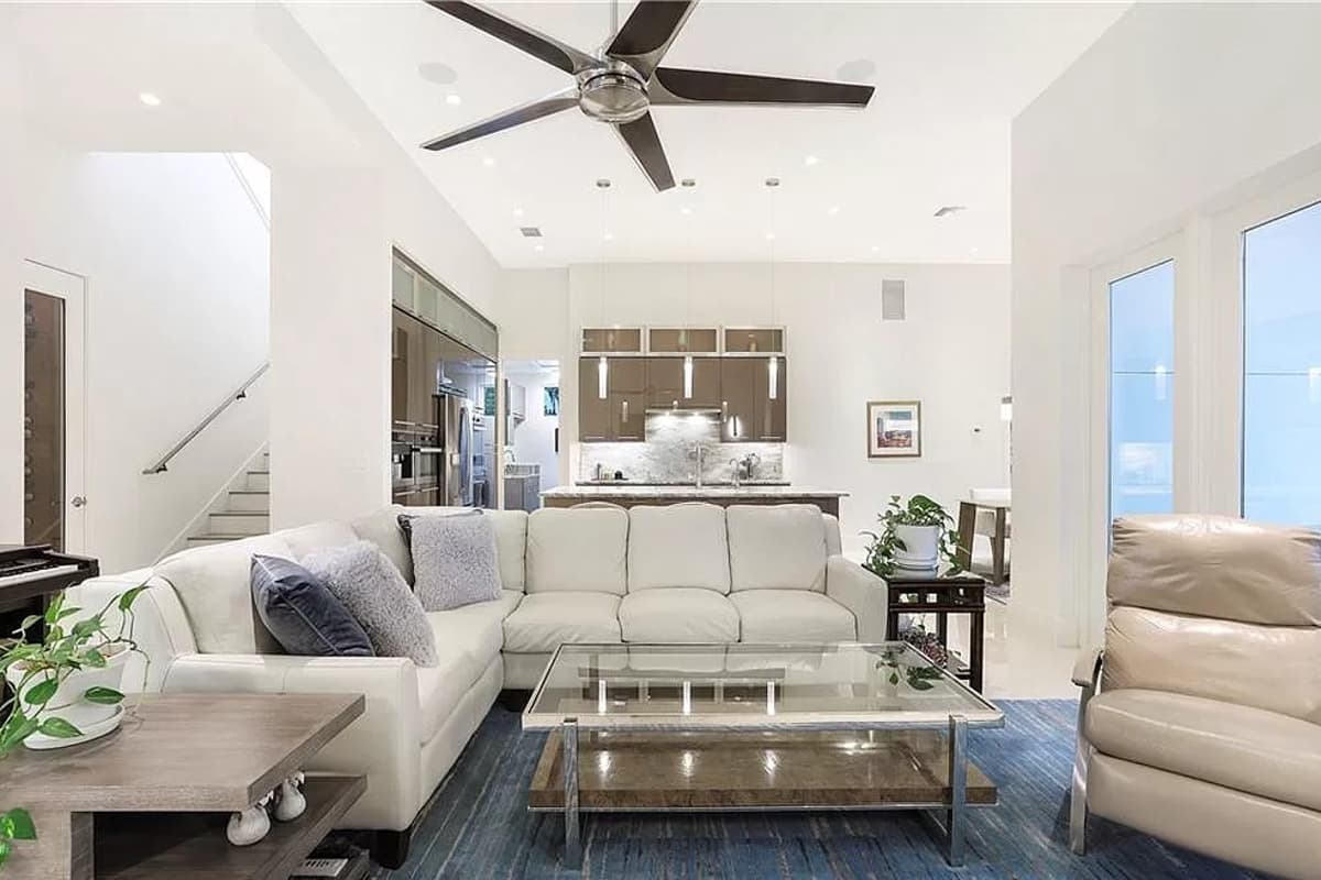 Living room with sectional sofa, glass coffee table, and open view to kitchen with island and sleek cabinetry.