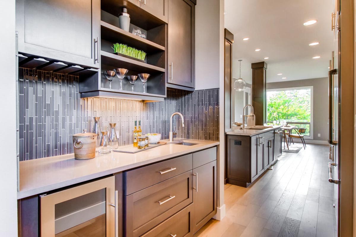 Modern wet bar with dark cabinetry, mosaic tile backsplash, sink, wine rack, and undercounter beverage cooler.