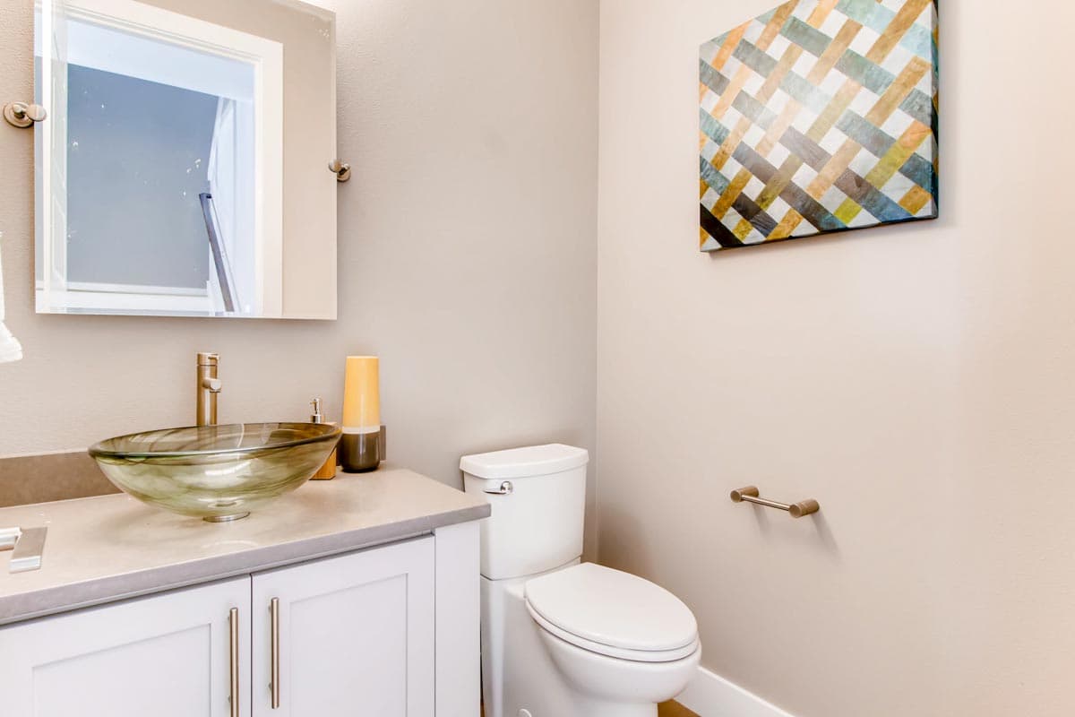 Powder room with vessel sink, vanity, toilet, and abstract art.