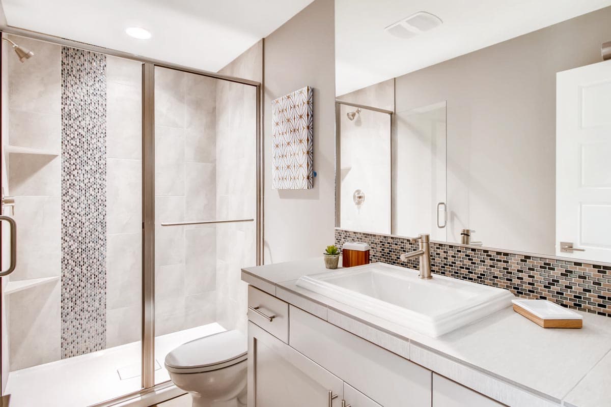 Modern bathroom with a glass-enclosed shower featuring mosaic tile accents and a vanity with a white rectangular sink.