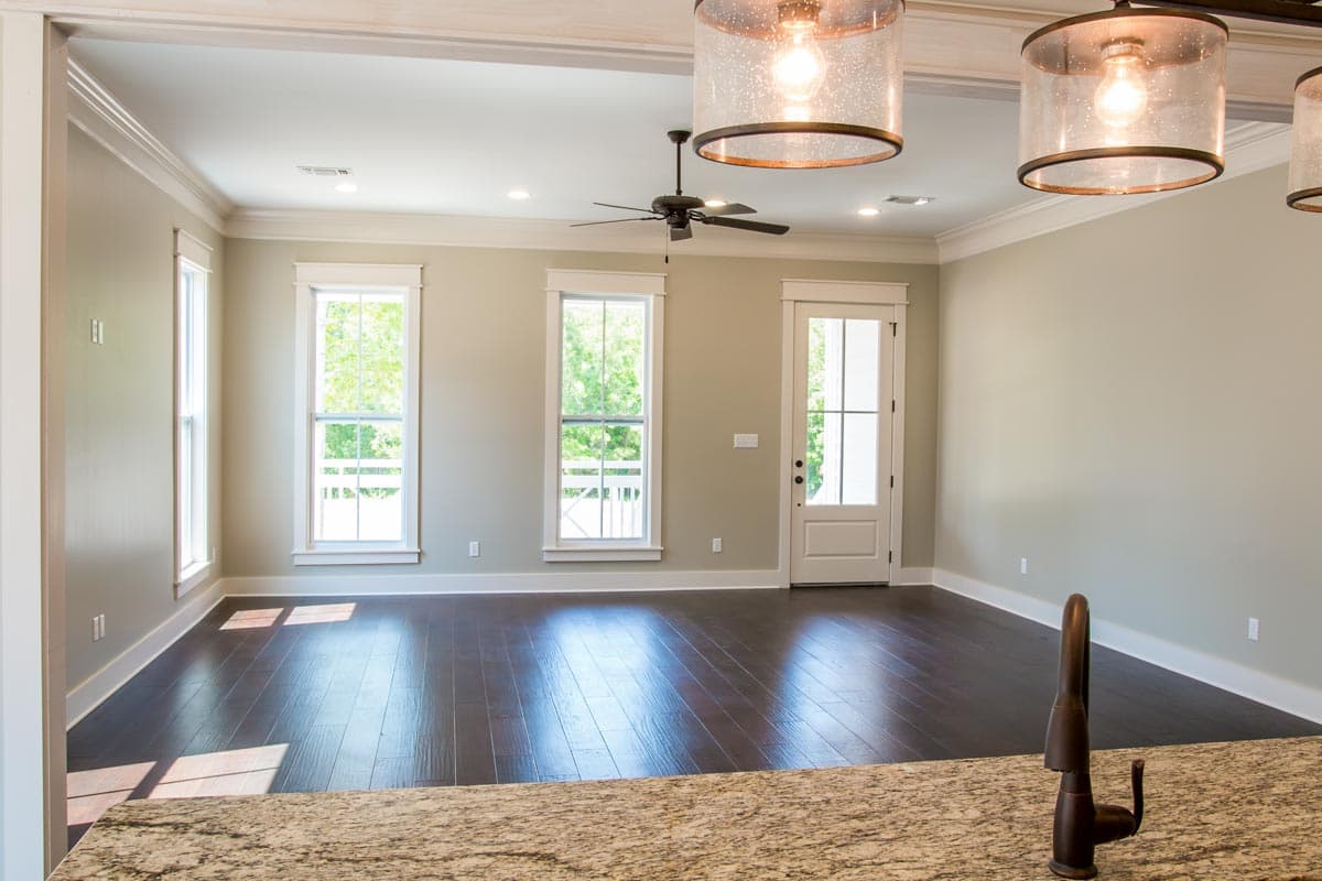 Interior view of living room with dark hardwood floors, three large windows, ceiling fan, and glass pendant lights.