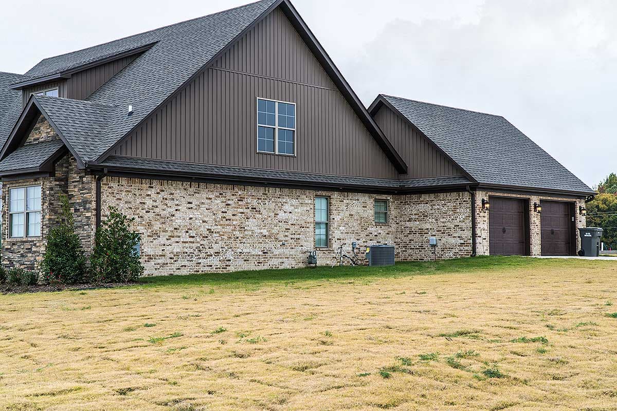 House plan exterior with brick and vertical siding, asphalt shingle roof, and a three-car garage.
