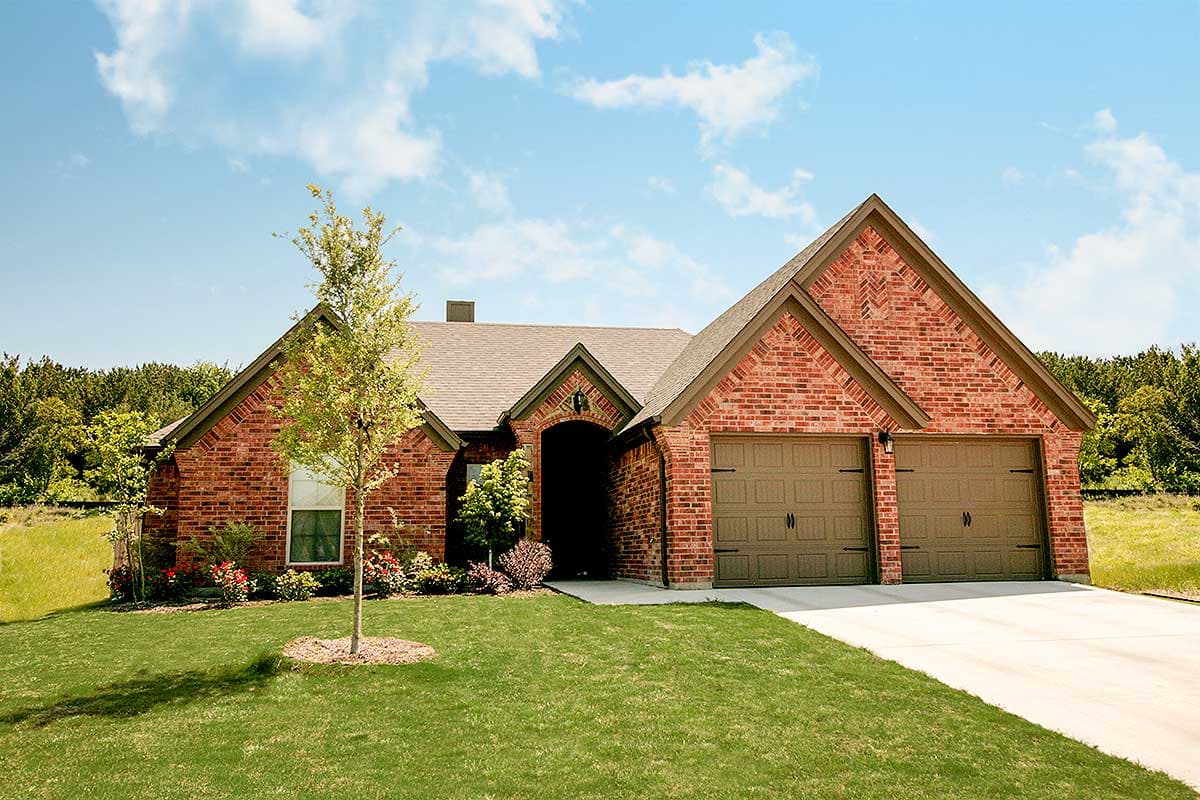 House plan exterior. One-story brick home with gabled roof, two-car garage, and arched entry. Features include a front lawn and mature trees.