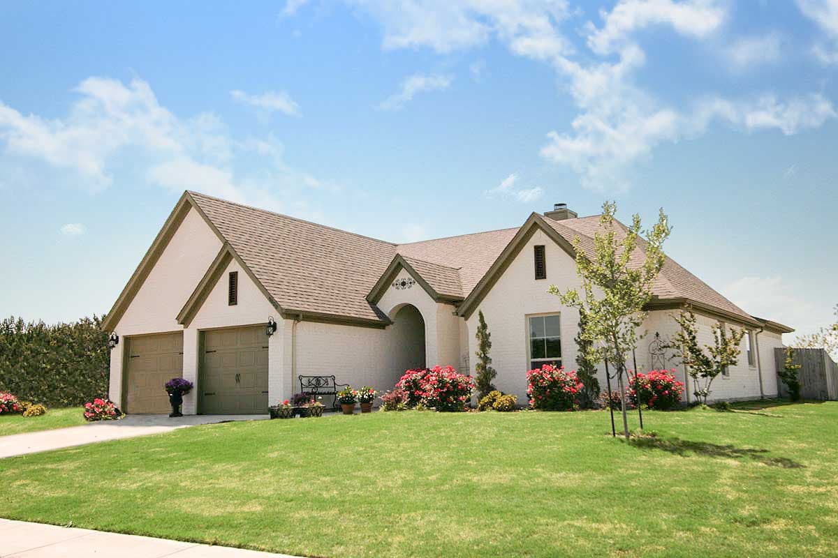 House plan exterior. Two-story, ranch-style home with multiple gables and a two-car garage. Features a covered entry and a brick facade.