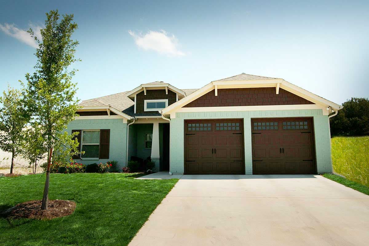 House plan exterior. Ranch-style home with two-car garage. Features include gabled roof, dormer, and front porch. Light green siding with brown trim.