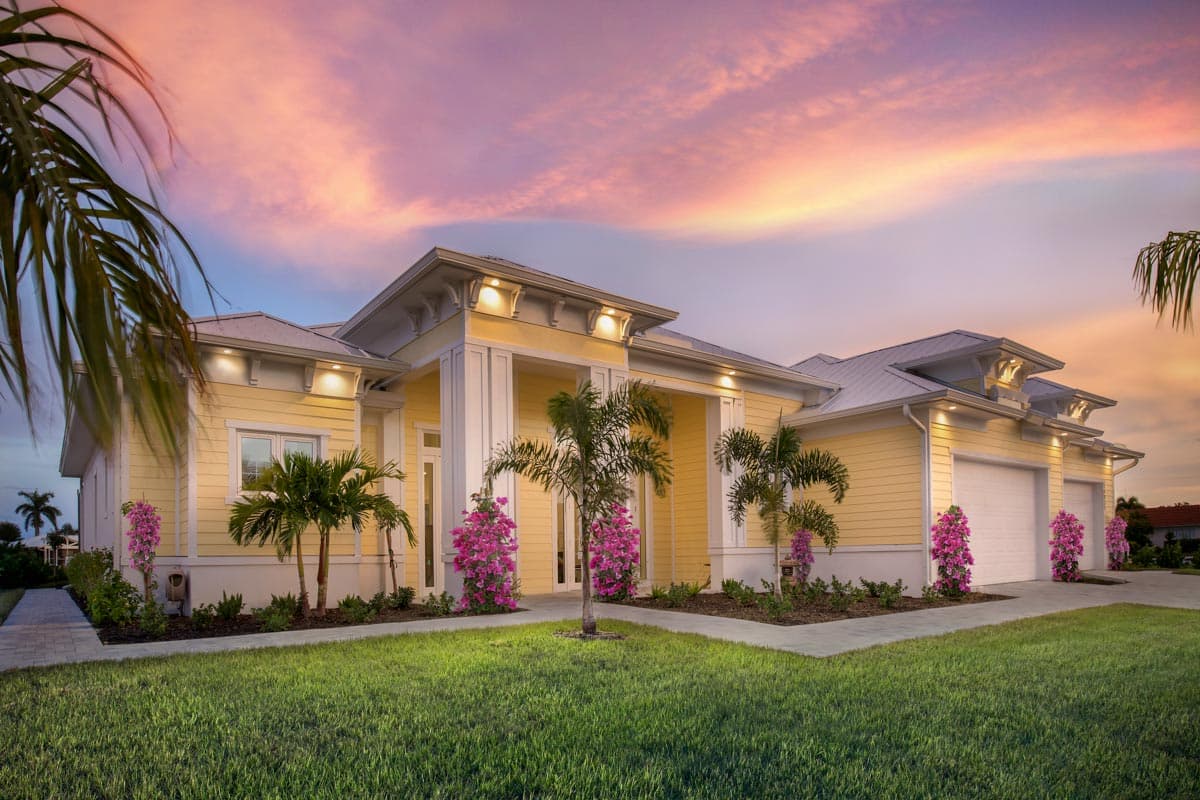 House plan exterior. Coastal-style home with columns, multiple gables, and a two-car garage. Features a low-pitched roof and landscaping.