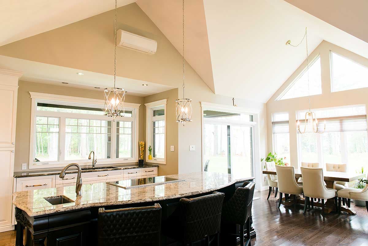 A modern kitchen with a large granite island and black leather bar stools, leading to a dining area with a long table and upholstered chairs.