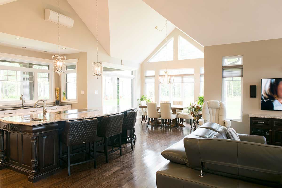 Spacious, modern living space featuring a kitchen island with bar stools, a dining area, a large sectional sofa, and tall windows.