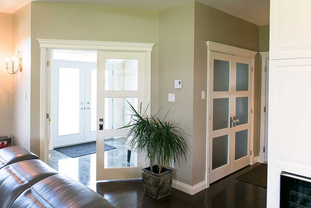 Interior doorway leading to an entryway with a plant, dark wood floors, and white trim doors. Another door has frosted glass panels.