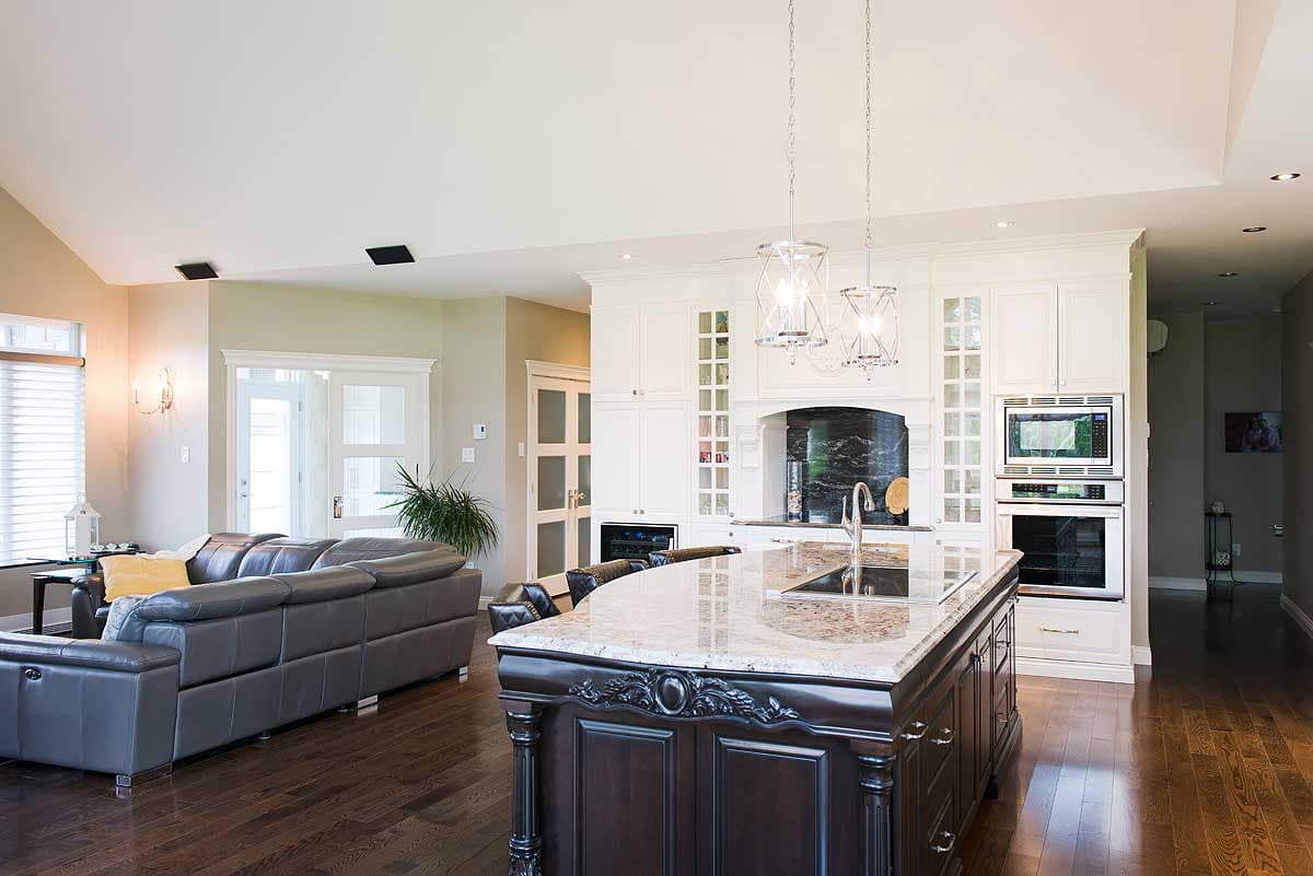 Spacious, open-concept kitchen and living area with a large island, dark cabinetry, and a gray leather sofa. Pendant lights hang above the island.