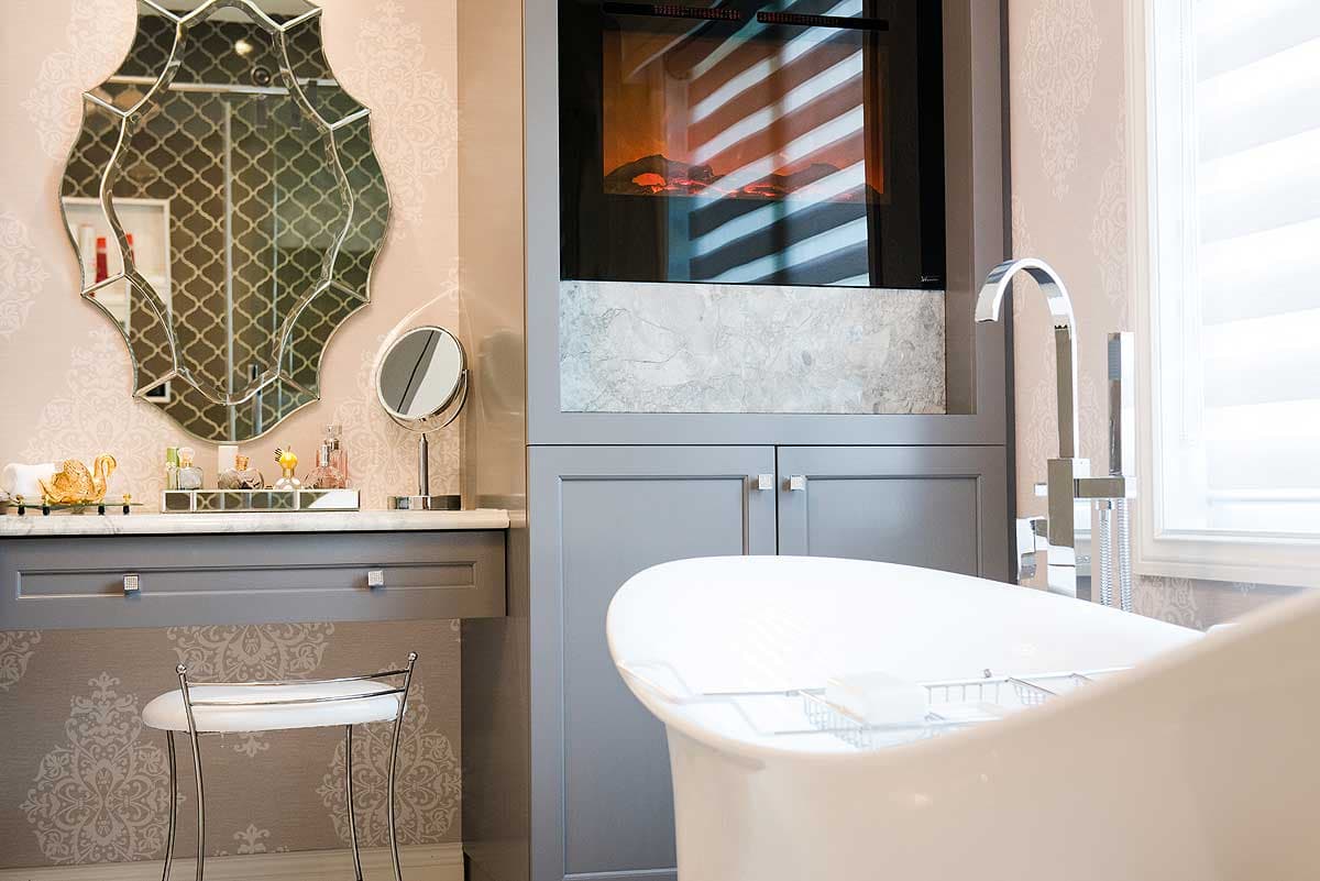 Elegant bathroom interior with a freestanding tub, fireplace, decorative mirror, and a vanity set. The space features stylish wallpaper.