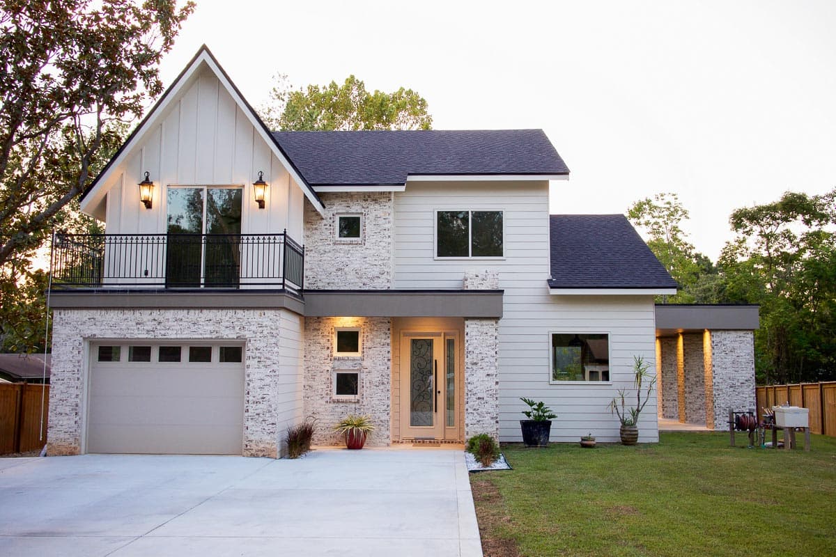 Two-story modern house plan exterior with white vertical siding, white brick accents, gabled roofline, balcony, and attached garage.