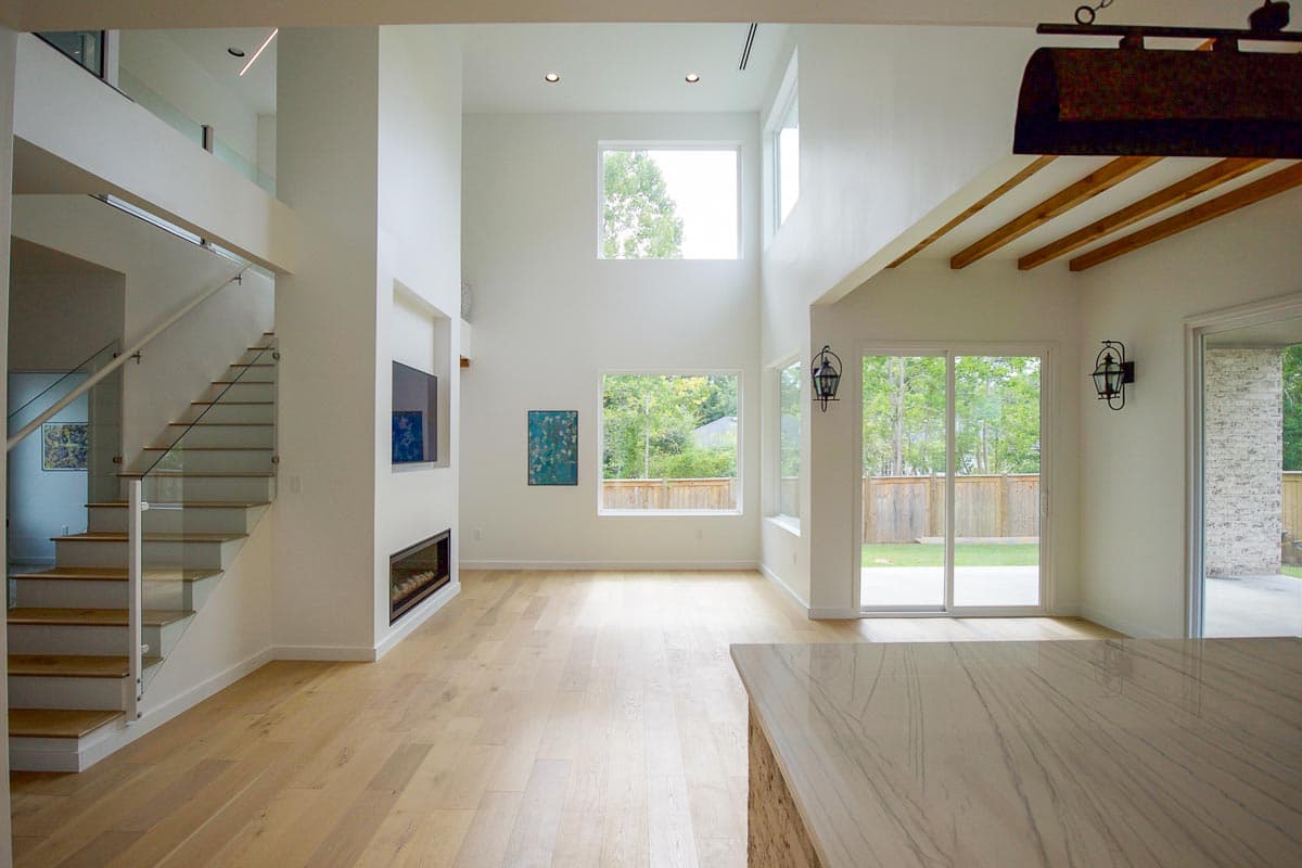 Modern interior with open layout, double-height ceiling, linear fireplace, glass-railed stairs, and large windows.